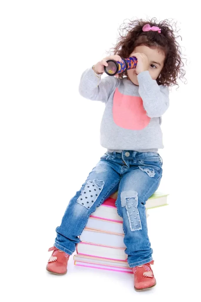 little girl sitting on a stack of books looking through a kaliedoscope